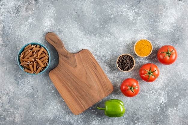 Pila di pasta dietetica marrone su sfondo grigio con verdure e spezie.