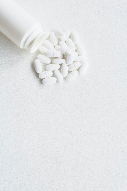 Pillole bianche e bottiglia di plastica su fondo bianco