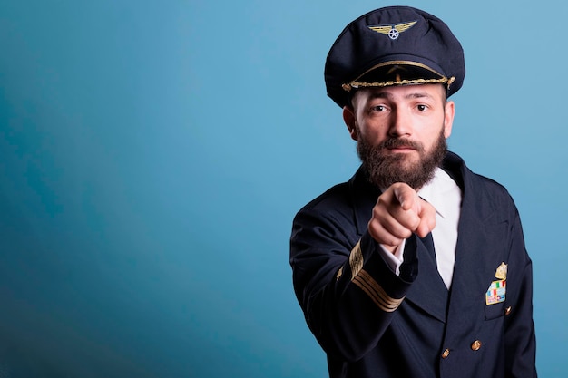 Pilota di aeroplano serio che punta alla telecamera, reclutamento dell'accademia di aviazione, capitano dell'aereo che indossa l'uniforme e ritratto di vista frontale del cappello. Aviatore di mezza età con stemma delle ali della compagnia aerea sulla giacca