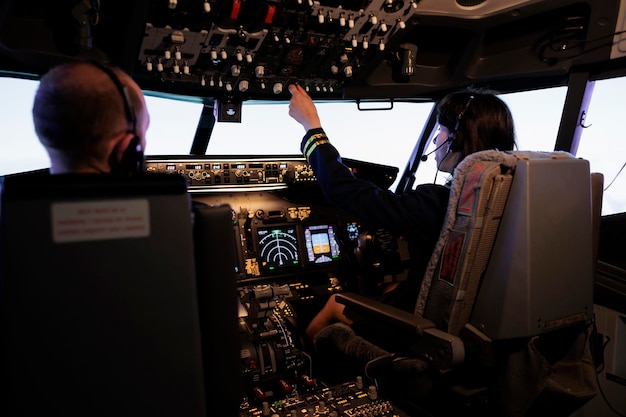 Pilota femminile che assiste il capitano al decollo e al volo dell'aereo, utilizzando i pulsanti sul comando del cruscotto nella cabina di pilotaggio. Aerei di linea jet aereo con parabrezza di navigazione e pannello di controllo.