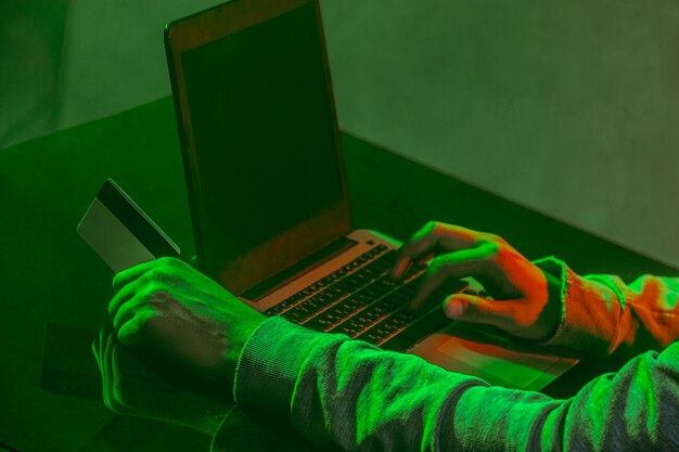 Pirata informatico di computer incappucciato che ruba informazioni con il computer portatile