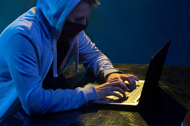 Pirata informatico di computer incappucciato che ruba informazioni con il computer portatile