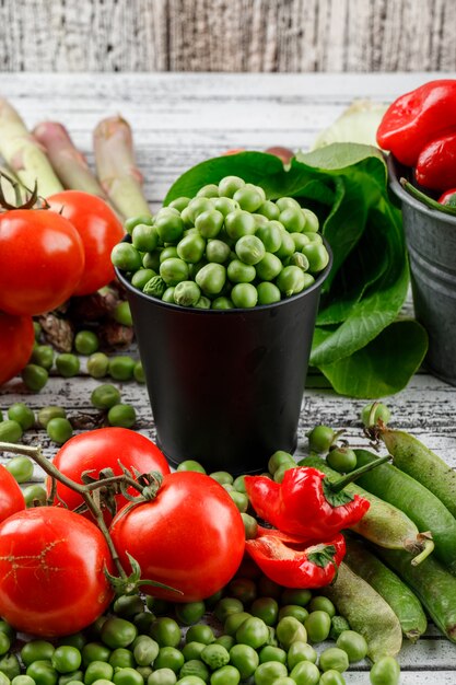 Piselli in un mini secchio con peperoni, pomodori, asparagi, cavolo cinese, vista dall'alto di baccelli verdi su una parete di legno sgangherata