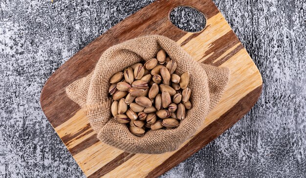 Pistacchi di vista superiore in sacco sul tagliere sull'orizzontale grigio di struttura