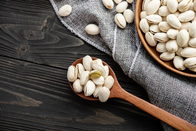 Pistacchi in un cucchiaio di legno. Ciotola di legno con pistacchi di noci. su uno sfondo di legno, vicino a una borsa di tela da imballaggio. Cibo sano e spuntino, cibo vegetariano biologico.