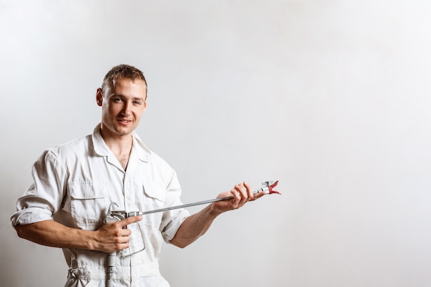 Pistola a spruzzo della tenuta del lavoratore sulla parete bianca.