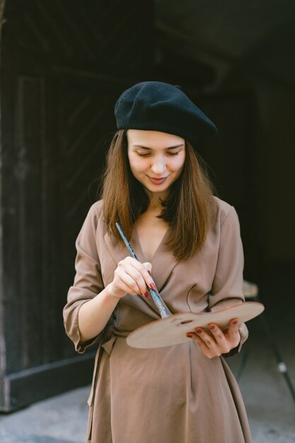 Pittore femminile che dipinge in città. Una donna che indossa un abito color cachi e un cappello nero