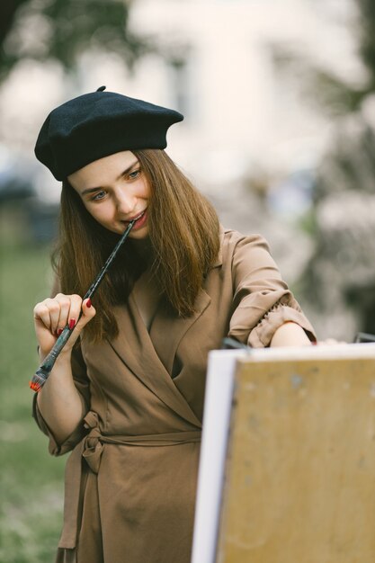 Pittore femminile che dipinge nel parco. Una donna che indossa un abito color cachi e un cappello nero