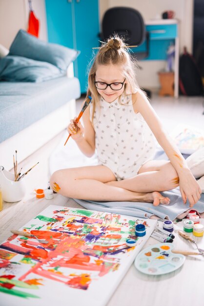 Pittura graziosa della ragazza con la gouache sul pavimento