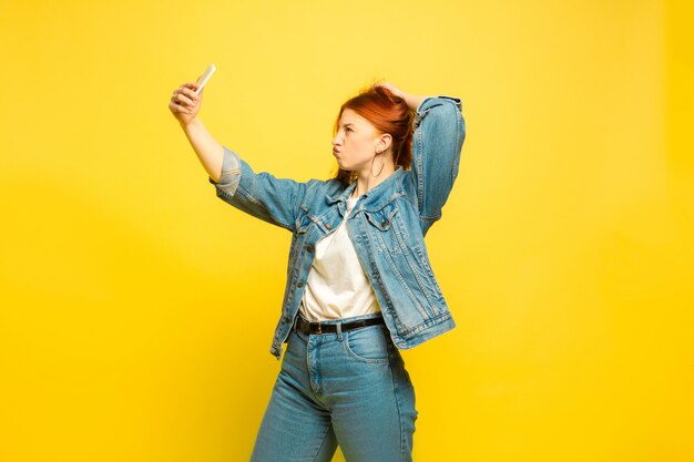 È più facile essere follower. Hai bisogno di vestiti minimi per i selfie. Ritratto della donna caucasica su sfondo giallo. Bello modello femminile dei capelli rossi. Concetto di emozioni umane, espressione facciale, vendite, annuncio.