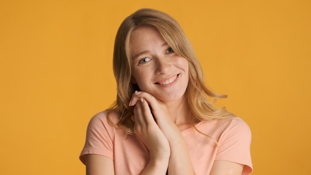 Piuttosto affascinante ragazza bionda che tiene le mani nera faccia carinamente guardando nella fotocamera isolata su sfondo giallo