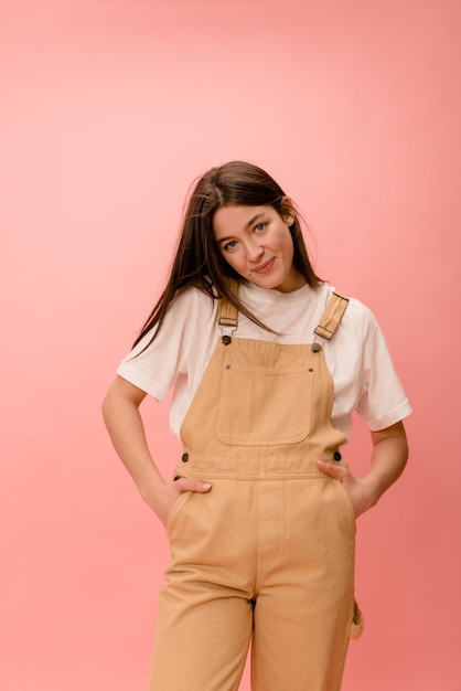 Piuttosto giovane donna bruna caucasica che guarda modestamente la fotocamera tenendo le mani nelle tasche della tuta in studio Concetto di svago per lo stile di vita