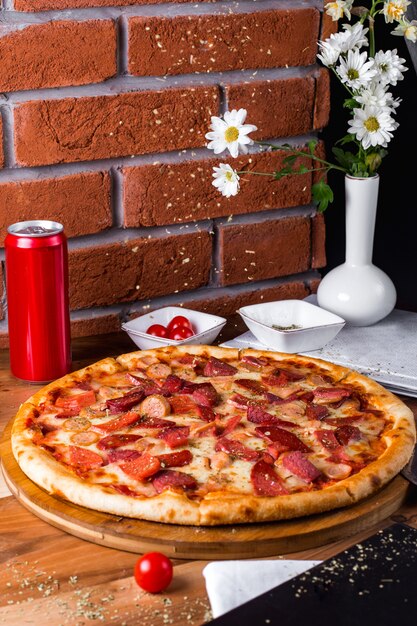 Pizza ai peperoni con pomodori e lattina di soda sul tavolo