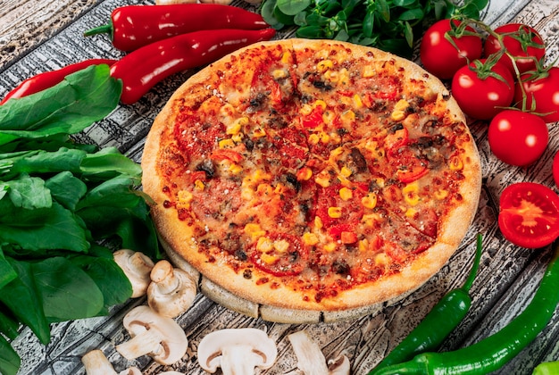 Pizza con i peperoni, i funghi, i pomodori, la pianta e le foglie di menta sul fondo leggero dello stucco, vista dell'angolo alto.