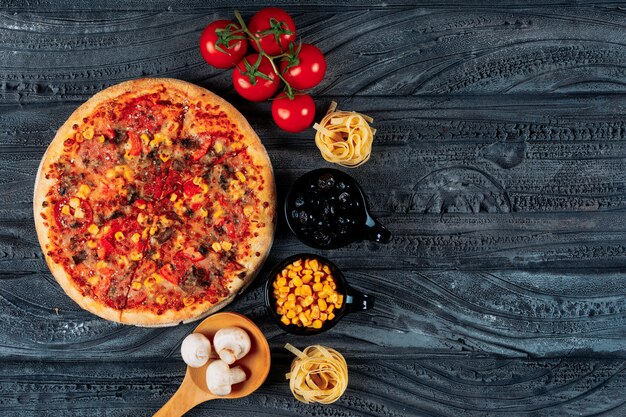 Pizza con pomodori, spaghetti, mais, olive, funghi vista dall'alto su uno sfondo blu scuro