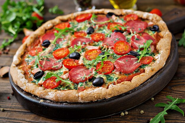 Pizza con salame, pomodori, olive e formaggio su un impasto con farina integrale. Cibo italiano.