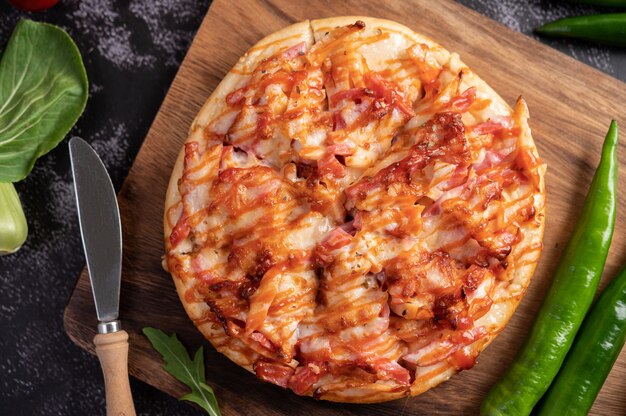 Pizza con salsiccia, mais, fagioli, gamberetti e pancetta su un piatto di legno