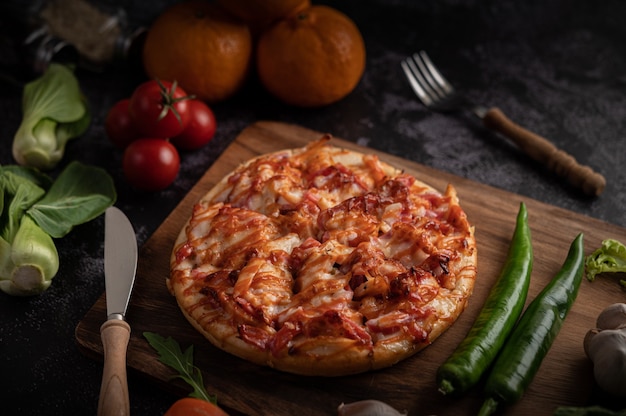 Pizza con salsiccia, mais, fagioli, gamberetti e pancetta su un piatto di legno