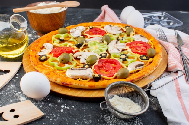 Pizza di funghi piccanti vista frontale con pomodori rossi peperoni olive tutte affettate all'interno con olio e farina su grigio
