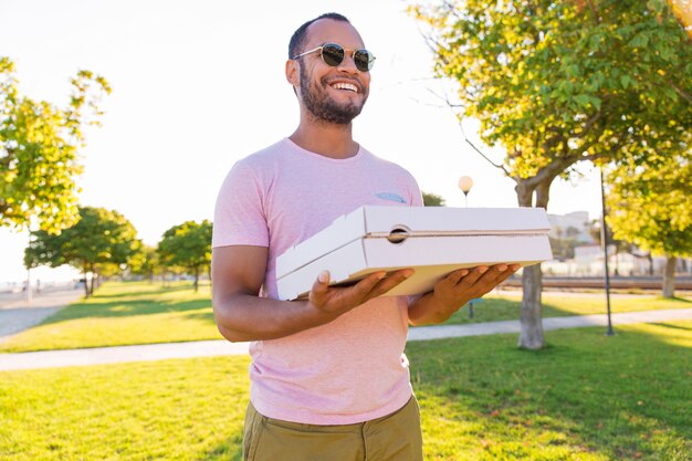 Pizza di trasporto del corriere maschio latino felice in parco