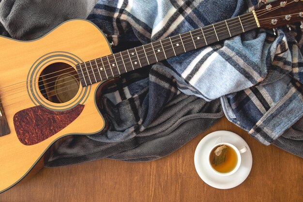 Plaid di chitarra acustica e una tazza di tè su una vista dall'alto di fondo in legno