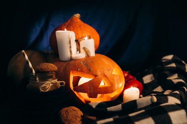 Plaid giace intorno a Halloween pumpking con candele lucenti intorno ad esso e una tazza di cioccolata calda con biscotti