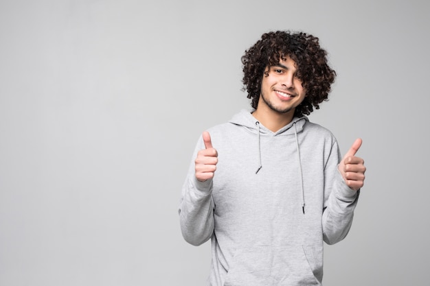 Pollice lshowing sorridente dell'uomo riccio su isolato su una parete bianca