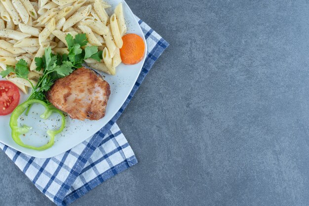 Pollo alla griglia e penne cremose sul piatto bianco.