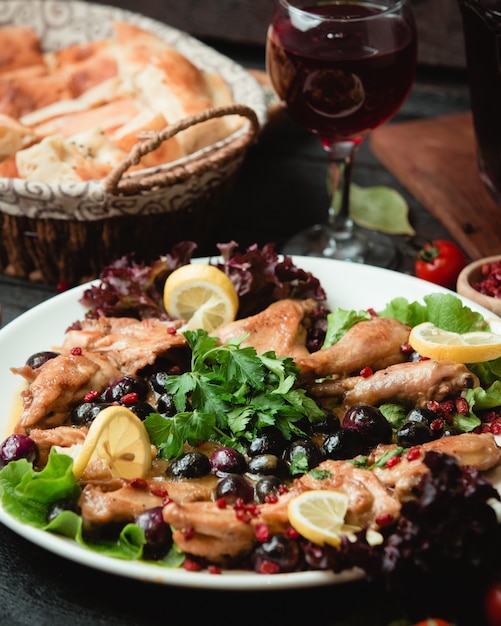 Pollo alla griglia servito con erbe verdi e fette di limone.