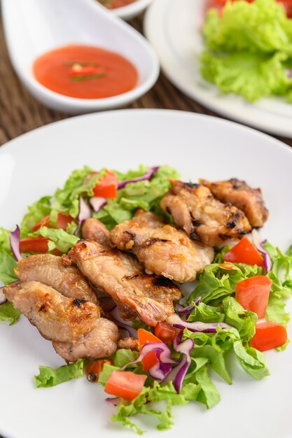 Pollo alla griglia su un piatto bianco con insalata di pomodori, carote e peperoncini tagliati a pezzi.