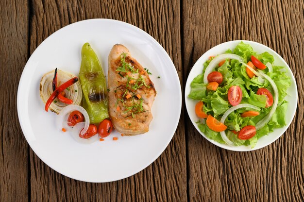 Pollo alla griglia su un piatto bianco con pomodori, insalata, cipolla, peperoncino e salsa.