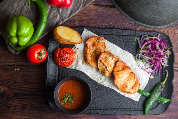 Pollo alla griglia vista dall'alto con orizzontale di pane pita, pomodoro, cipolla, pepe e salsa