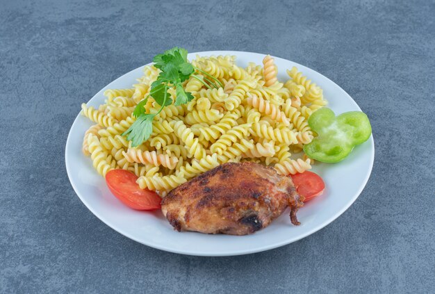 Pollo arrosto e fusilli sul piatto bianco.