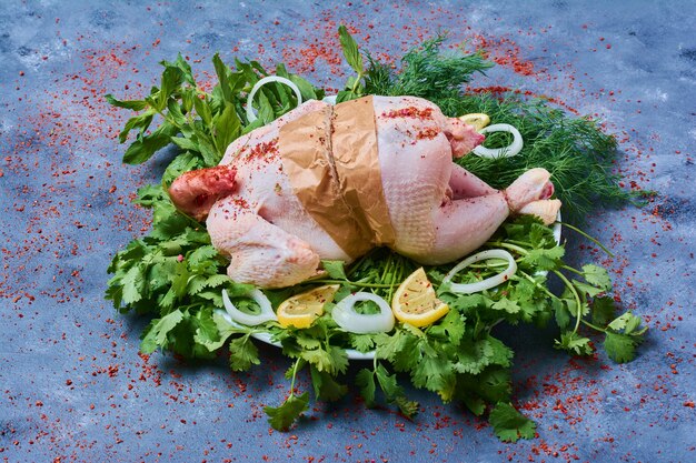 Pollo crudo con erbe su una tavola di legno sull'azzurro