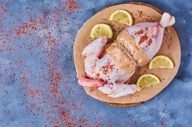 Pollo crudo con limone su una tavola di legno sull'azzurro