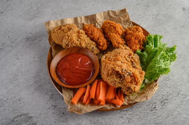 Pollo fritto croccante su un piatto di legno con salsa al pomodoro e carota