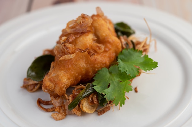 Pollo fritto dell'erba su un piatto bianco su un pavimento di legno.