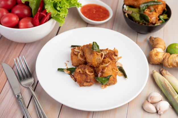 Pollo fritto dell'erba su un piatto bianco su un pavimento di legno.