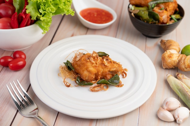 Pollo fritto dell'erba su un piatto bianco su un pavimento di legno.