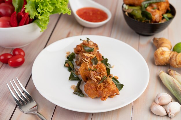 Pollo fritto dell'erba su un piatto bianco su un pavimento di legno.