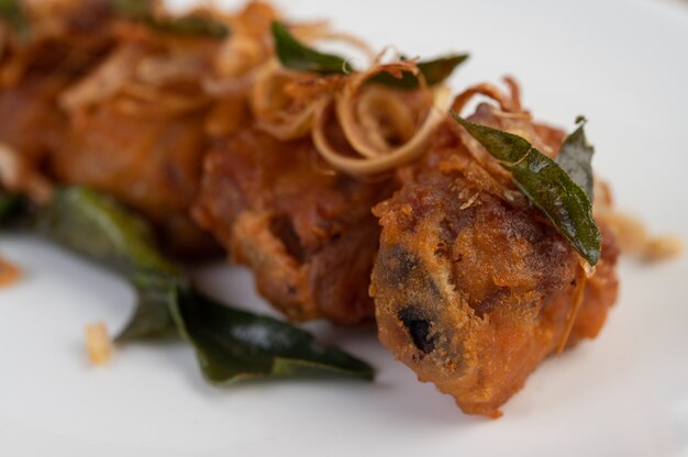 Pollo fritto dell'erba su un piatto bianco su un pavimento di legno.