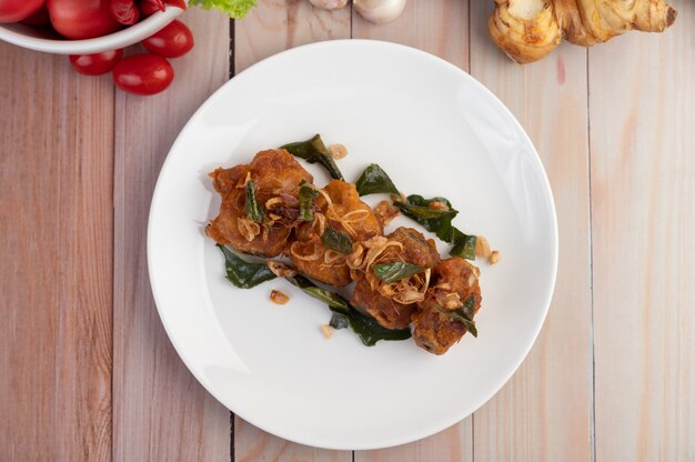 Pollo fritto dell'erba su un piatto bianco su un pavimento di legno.