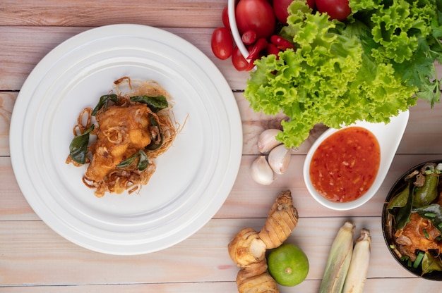 Pollo fritto dell'erba su un piatto bianco su un pavimento di legno.