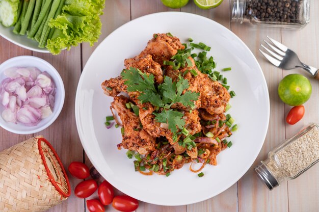 Pollo piccante tritato su un piatto bianco completo di cetrioli, lattuga e contorni.