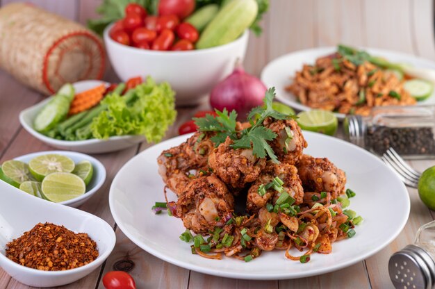 Pollo piccante tritato su un piatto bianco completo di cetrioli, lattuga e contorni.