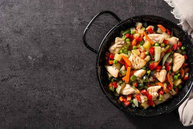 Pollo saltato in padella e verdure su sfondo di pietra nera