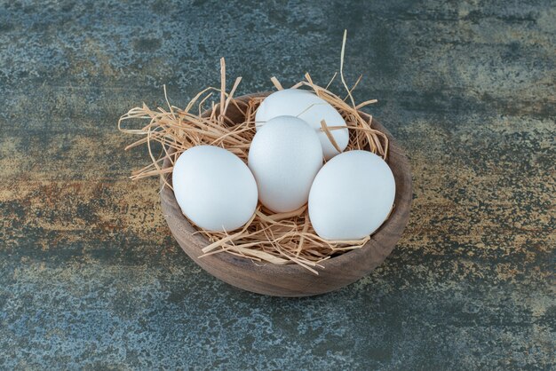 Pollo uova bianche fresche che si trovano nel fieno sulla ciotola di legno