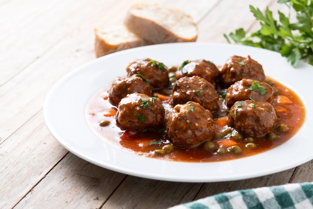 Polpette di carne, piselli verdi e carote con salsa di pomodoro su un tavolo di legno.