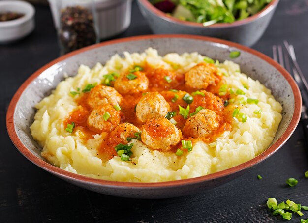 Polpette in salsa di pomodoro con purè di patate in ciotola.