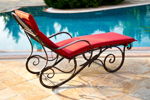 poltrona in ferro con cuscini rossi accanto alla piscina